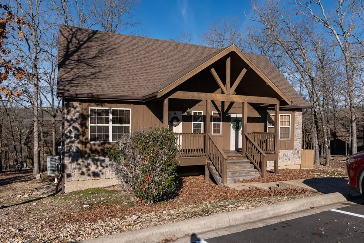 A cozy wooden porch with a stone foundation nestled among lush trees, featuring inviting seating perfect for relaxing and enjoying nature. The tranquil setting suggests both privacy and a strong connection to the outdoors, ideal for morning coffee or an intimate evening conversation.