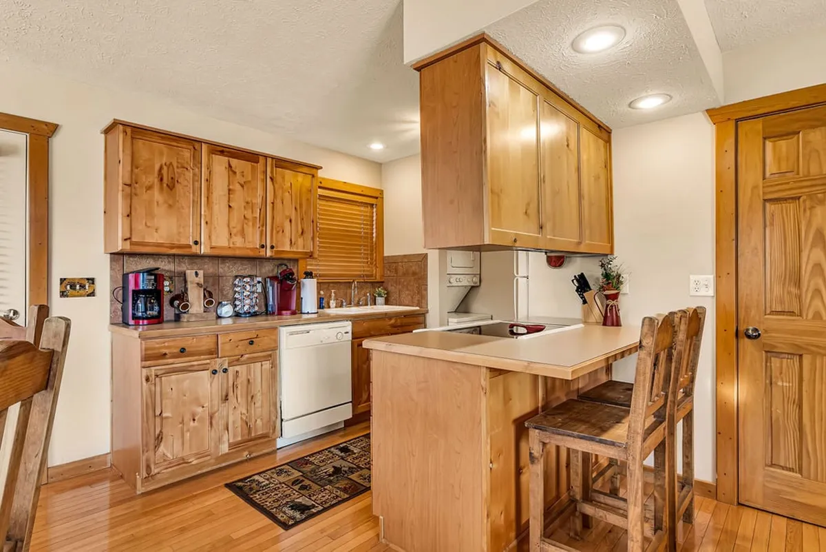 A cozy kitchen with wooden cabinetry, a central island with bar stools, and gleaming stainless appliances. The space is warm and inviting, with plenty of counter space for meal prep and comfortable seating for casual gatherings. Natural light filters in, highlighting the workspace and making it ideal for both family breakfasts and evening dinners.
