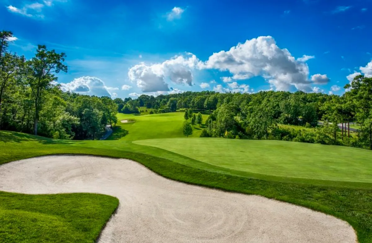 A panoramic view of a rolling golf course with bright green grass, a sand trap, and wide blue skies above. The landscape invites guests to participate in golf or enjoy peaceful walks surrounded by nature, embodying the year-round activities available at the resort.