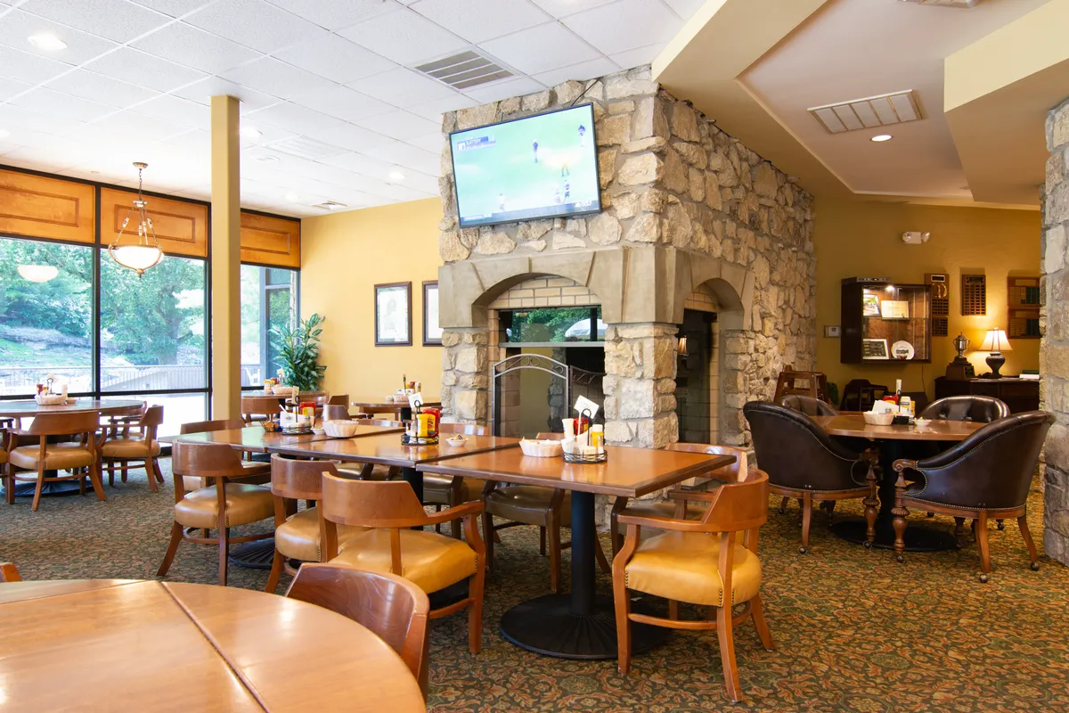 A comfortable interior dining area with a large stone fireplace, wooden tables, big windows, and cozy seating. The warm atmosphere is perfect for a relaxed dinner or casual gathering after a day of adventure.