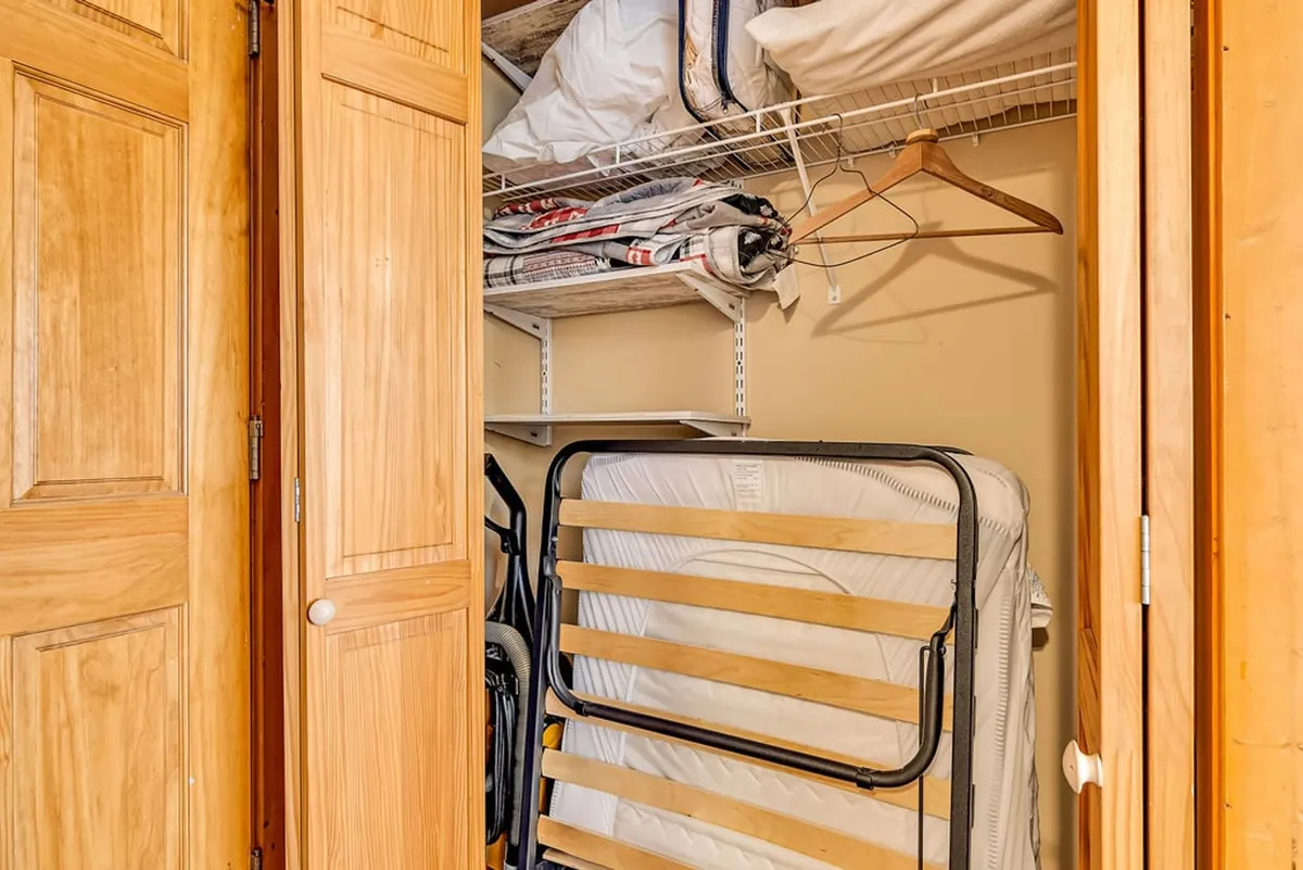 A practical closet area with wooden doors, stacked extra bedding, and a foldable bed frame, highlighting storage options and flexible sleeping arrangements for guests.
