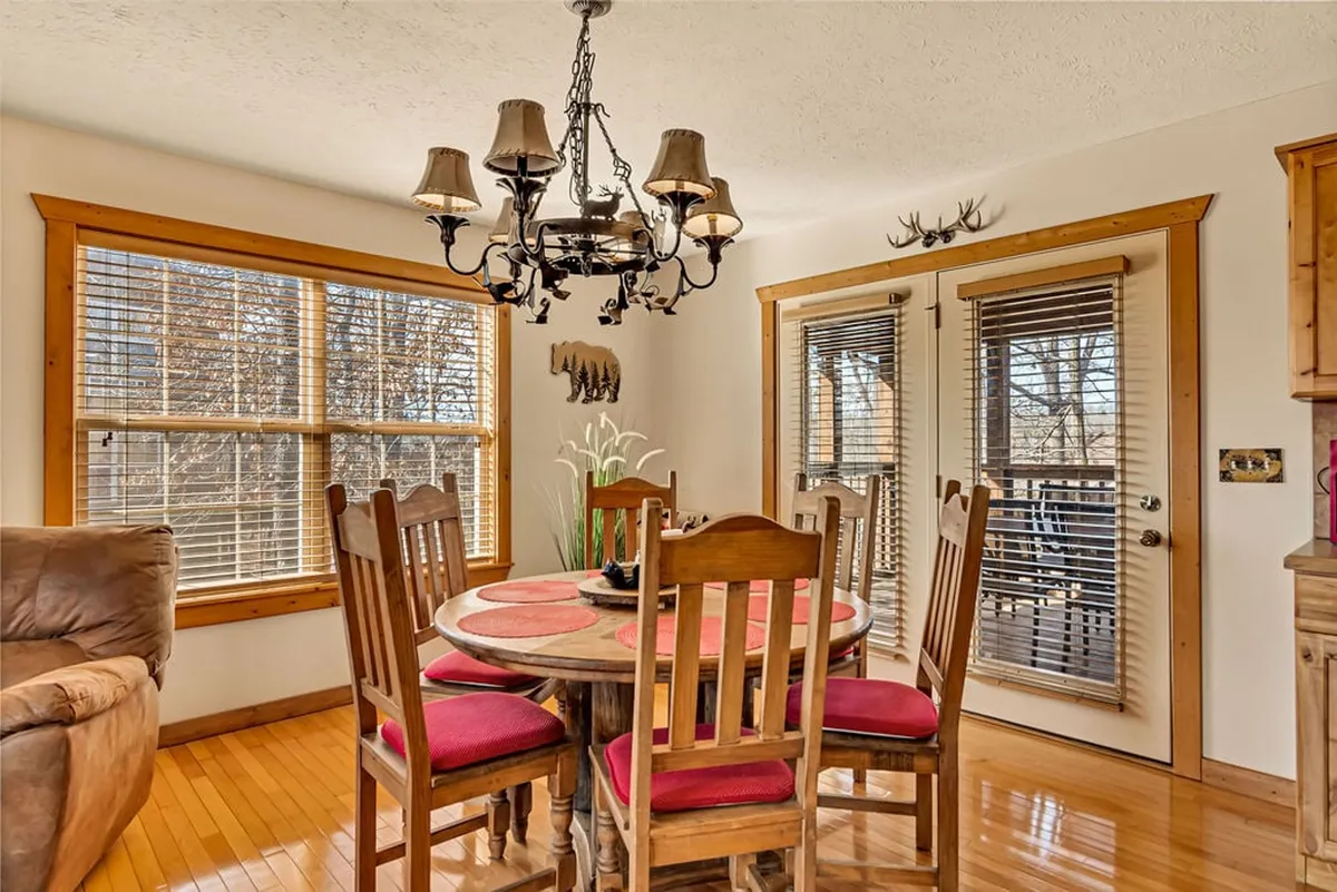 An inviting dining area featuring a sturdy wooden table set beneath a glowing chandelier, with windows offering natural light. The space is designed for family meals, social gatherings, and intimate dinners, echoing the warmth and camaraderie described in the section.