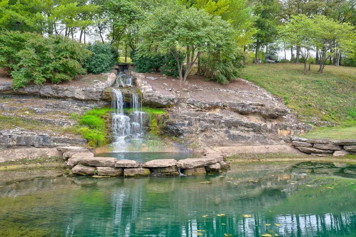 A tranquil exterior view featuring a cascading waterfall surrounded by rock formations, a serene pond, and lush trees. The natural setting is ideal for peaceful walks and outdoor relaxation, and the gentle water and greenery create a scenic, pet-friendly atmosphere.