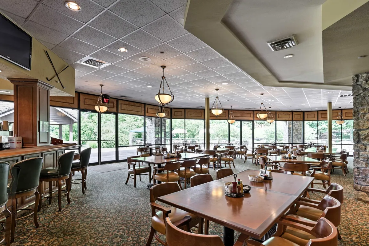 A welcoming clubhouse restaurant interior, featuring tables and chairs, large windows with plenty of natural light, and a relaxed, sociable atmosphere. The setting is perfect for meals with a view or casual gatherings.
