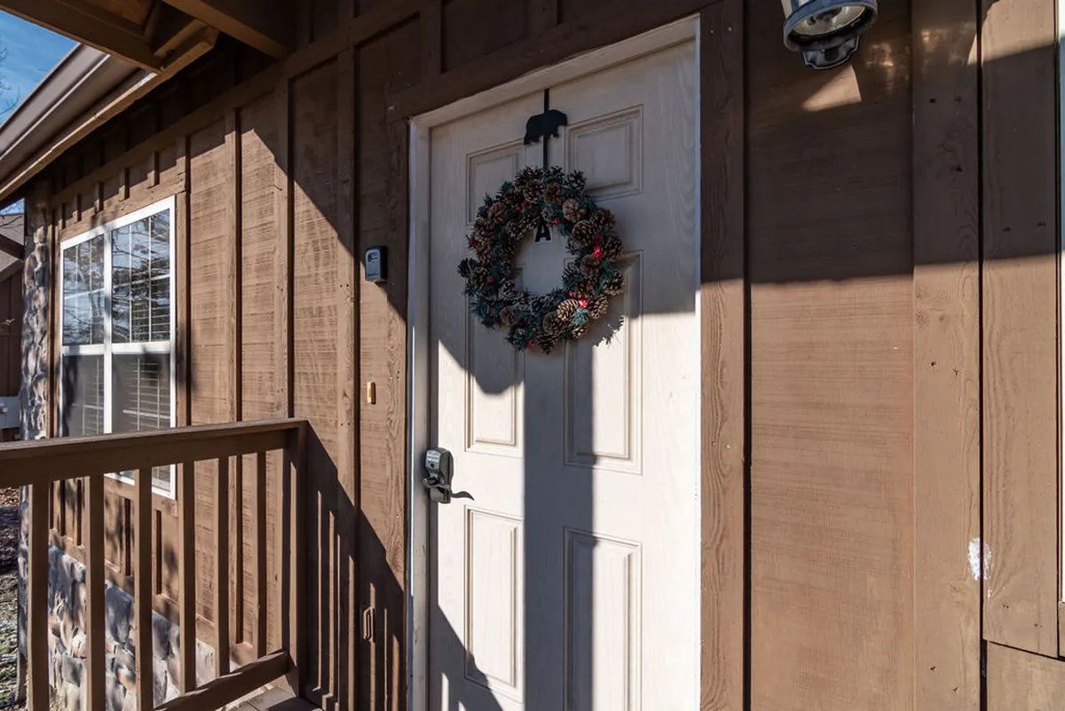 A cozy exterior shot of a front door with a decorative wreath, wooden siding, and a window, suggesting a warm welcome. The porch area is inviting and hints at comfortable, home-like spaces where guests and pets can relax after outdoor adventures.