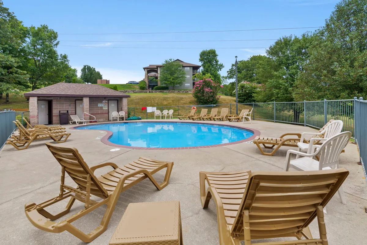 A lively, sunlit outdoor swimming pool surrounded by loungers and a poolside cabana, set amid lush greenery. The inviting pool area is ideal for families to relax, swim, and play together during the warmer months.