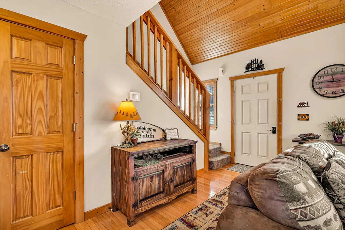 A cozy entryway featuring a wooden staircase, a welcome sign, a table lamp, and a couch. The area feels inviting and sets the stage for a warm, communal stay.
